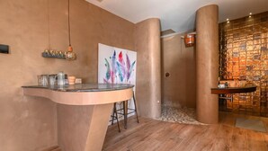 Een moderne badkamer met een gebogen wastafel, een grote spiegel en een decoratieve wand met een mozaïekpatroon.