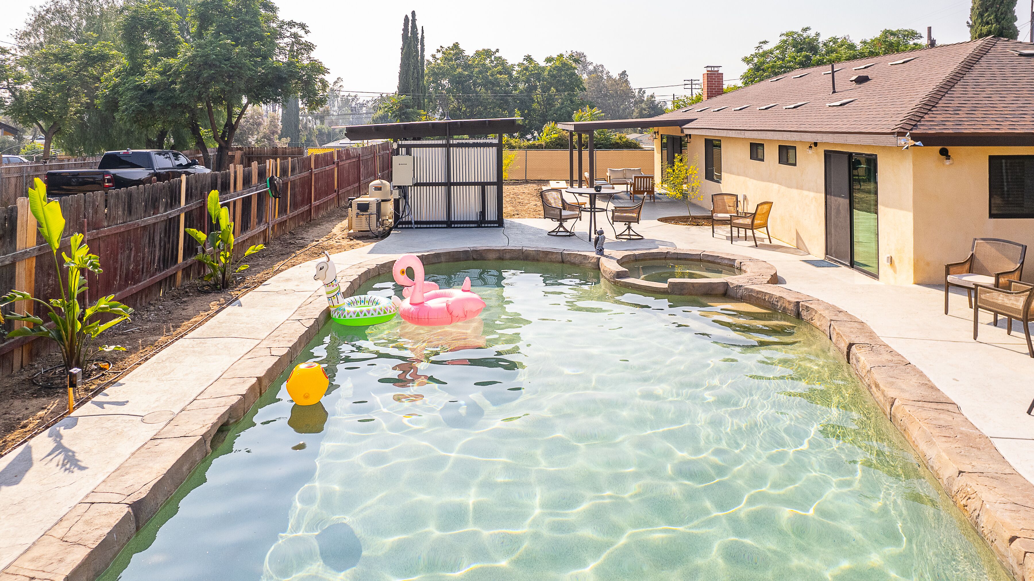 A clear swimming pool with inflatable toys, a fenced yard, and outdoor furniture.
