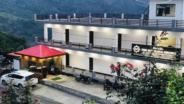 A hotel with a red-roofed entrance, a sign for "The Himalaya Orchid Hotel," and a view of the surrounding landscape. - Hotel The Himalaya Orchid Guptkashi (Ukhimath)