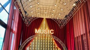 A room with a stage featuring a 'MUSIC' sign, red curtains, and a grid ceiling with lights. There are white chairs and tables arranged around the room. - Luxurious Suites in Kl Centre (Kuala Lumpur)