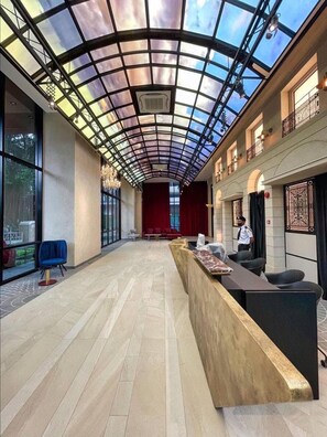 Enter a spacious lobby with a high ceiling, natural light pouring in through a glass panel design.