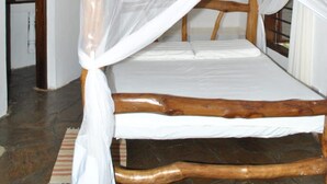 Una cama de madera con dosel blanco en una habitación con vigas de madera a la vista y suelo de baldosas.
