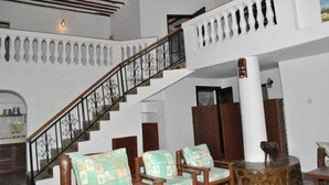 Un vestíbulo amplio con una imponente escalera, sillas de madera y un columnón decorativo.