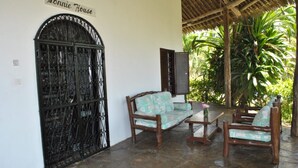 Un patio cubierto con una reja de hierro forjado que dice "Lonnie House", muebles de madera y abundante vegetación al fondo.