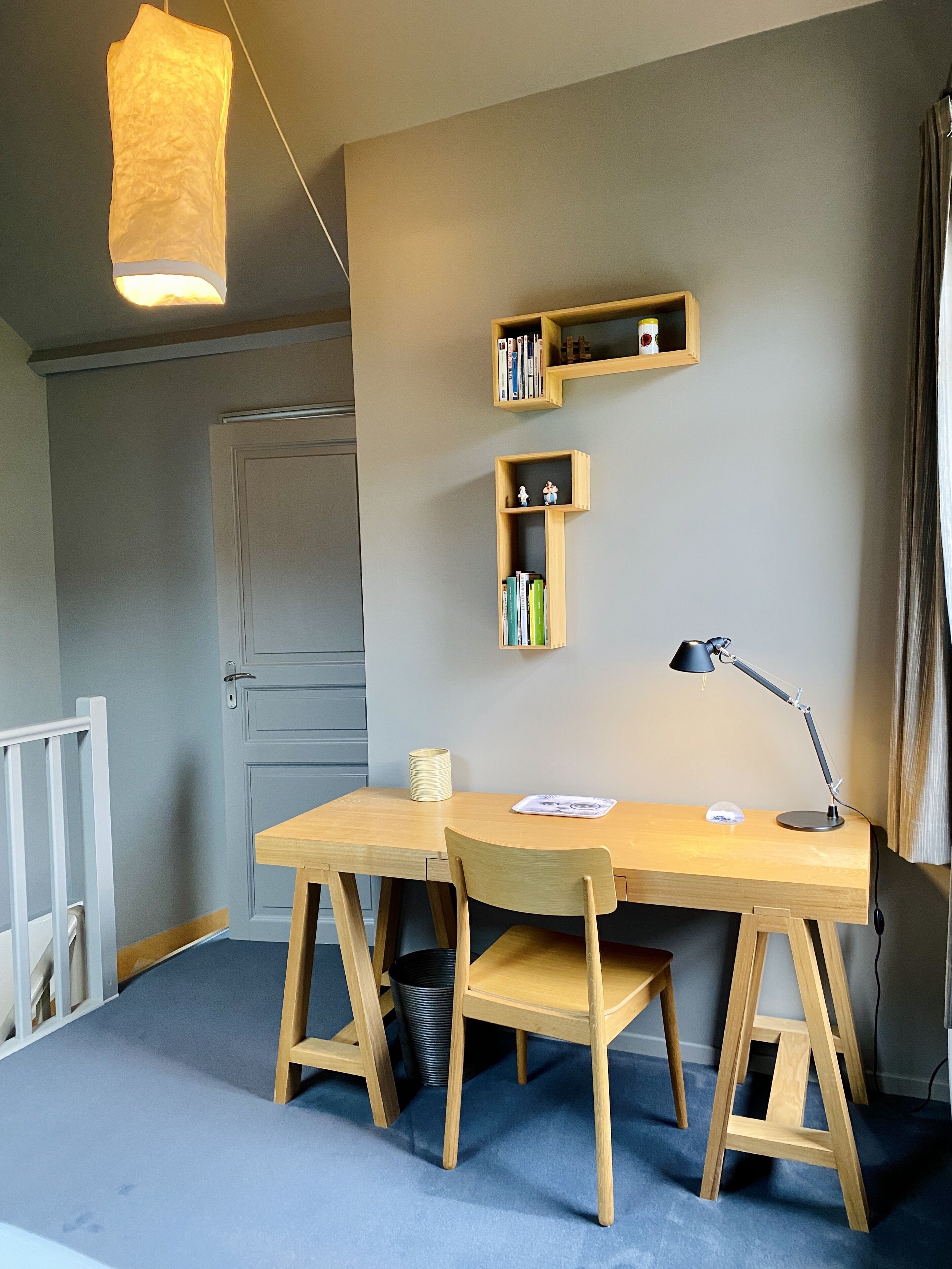 Una habitación con un escritorio de madera, dos sillas, una lámpara colgante y estanterías empotradas con libros y objetos decorativos.