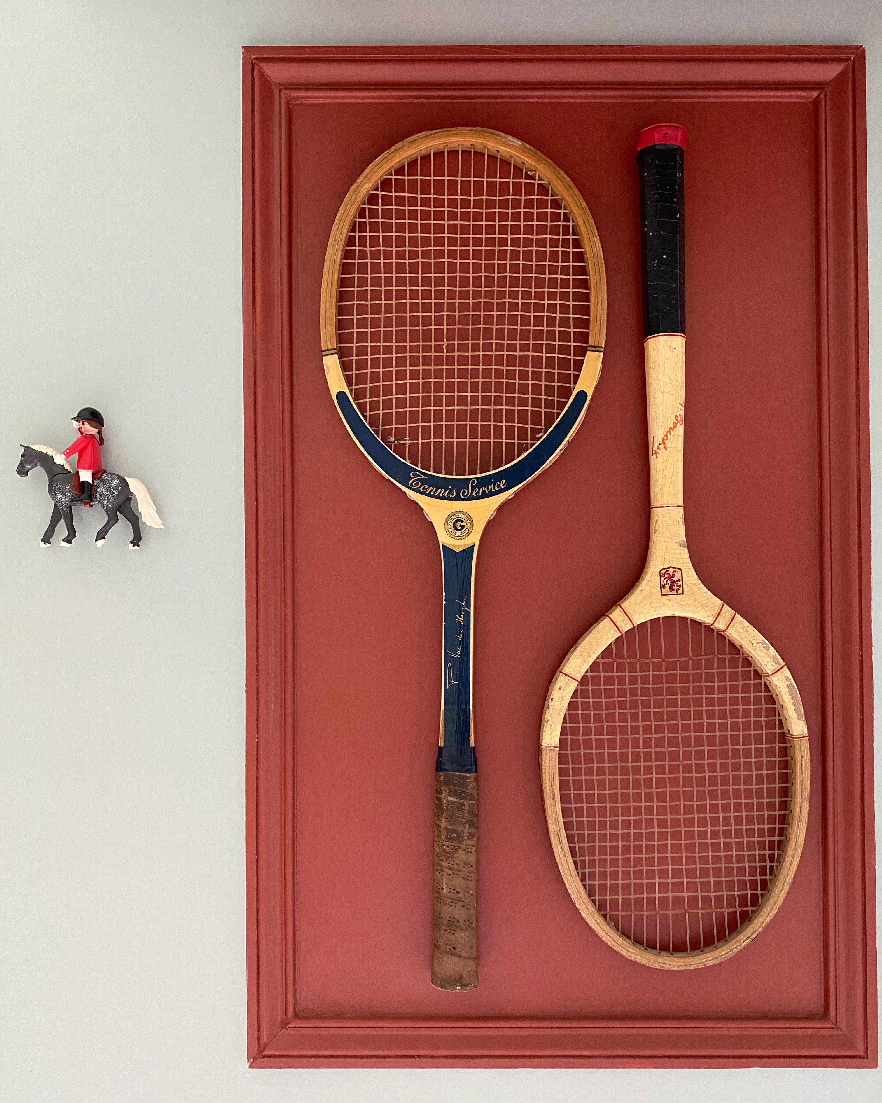 Dos raquetas de tenis y una figurita sobre una superficie roja.