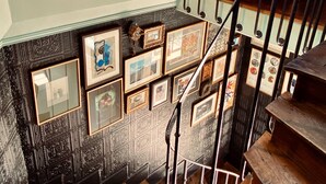 A staircase with a metal railing, a red chair, and a wall with framed pictures.