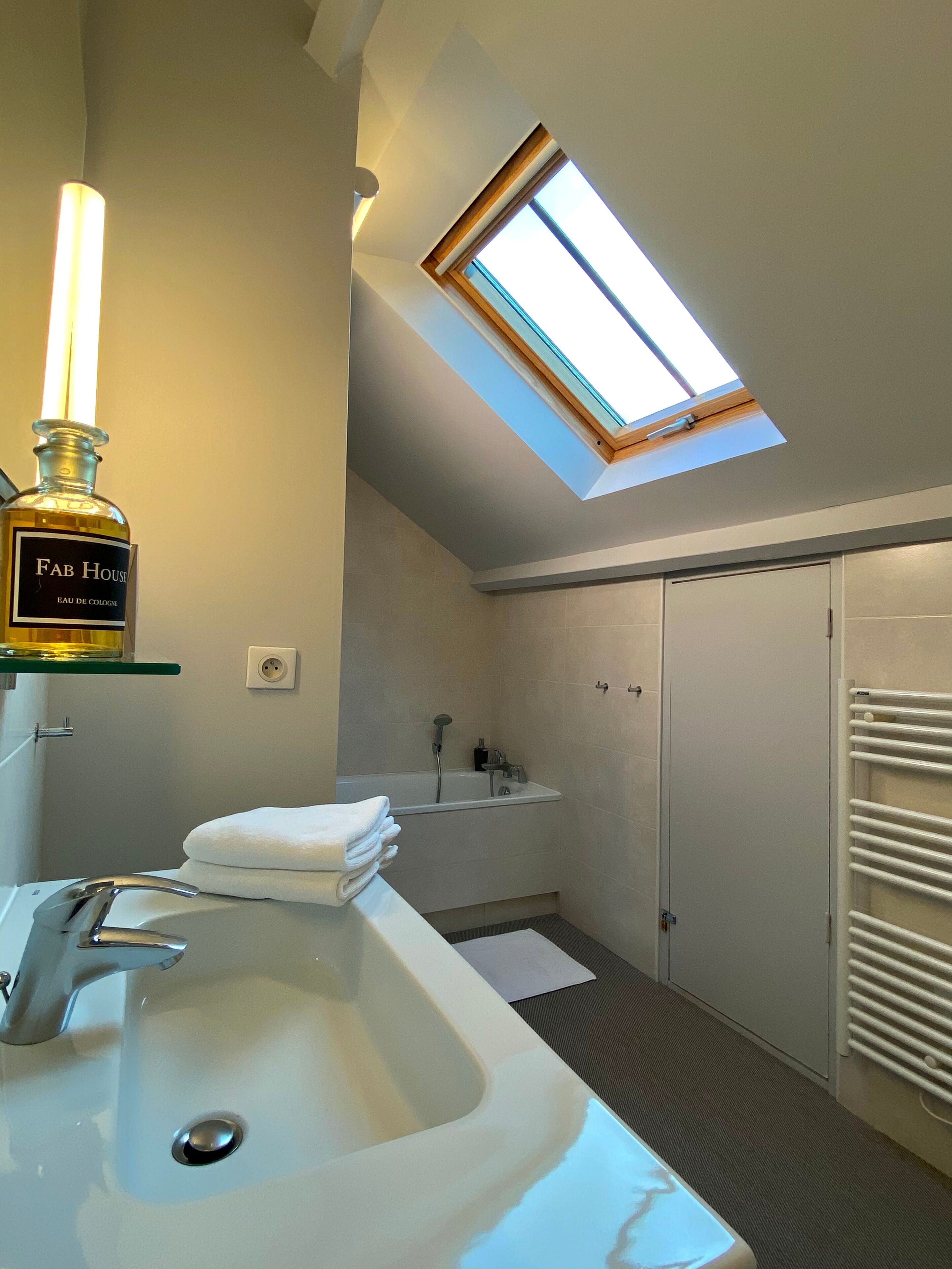 Un bagno moderno con una finestra a lucernario, un lavandino capiente e una bottiglia di colonia Fab House.