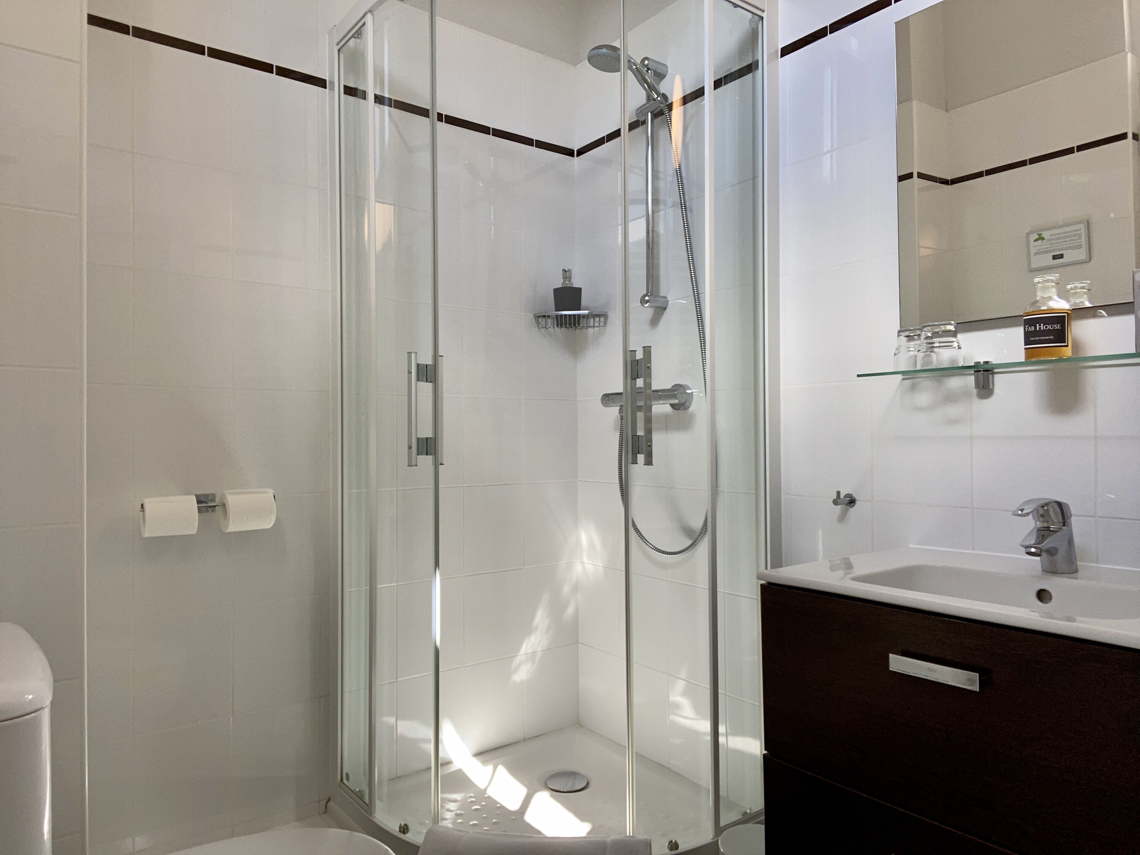 Un baño moderno con ducha acristalada, lavamanos blanco y tocador de tonos oscuros.