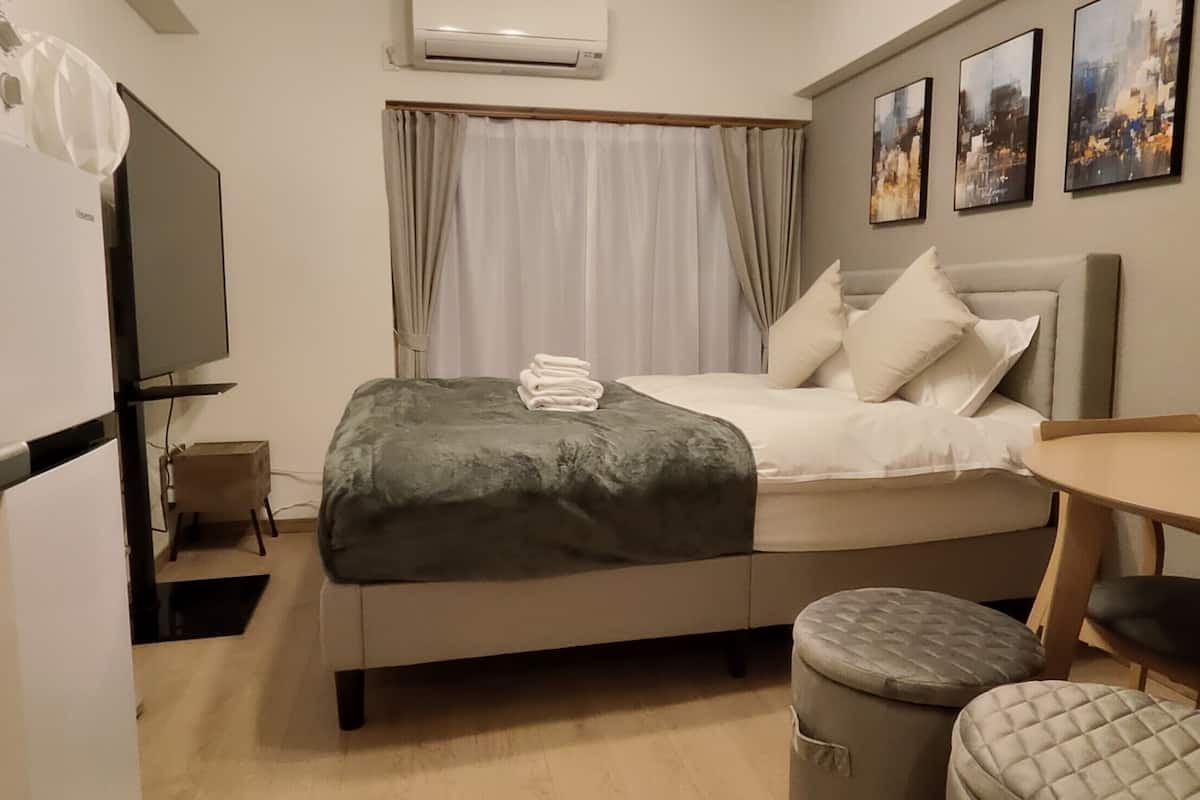 Une chambre d’hôtel de taille modeste, comprenant un lit, une petite table, une chaise, un téléviseur et une fenêtre avec des rideaux.