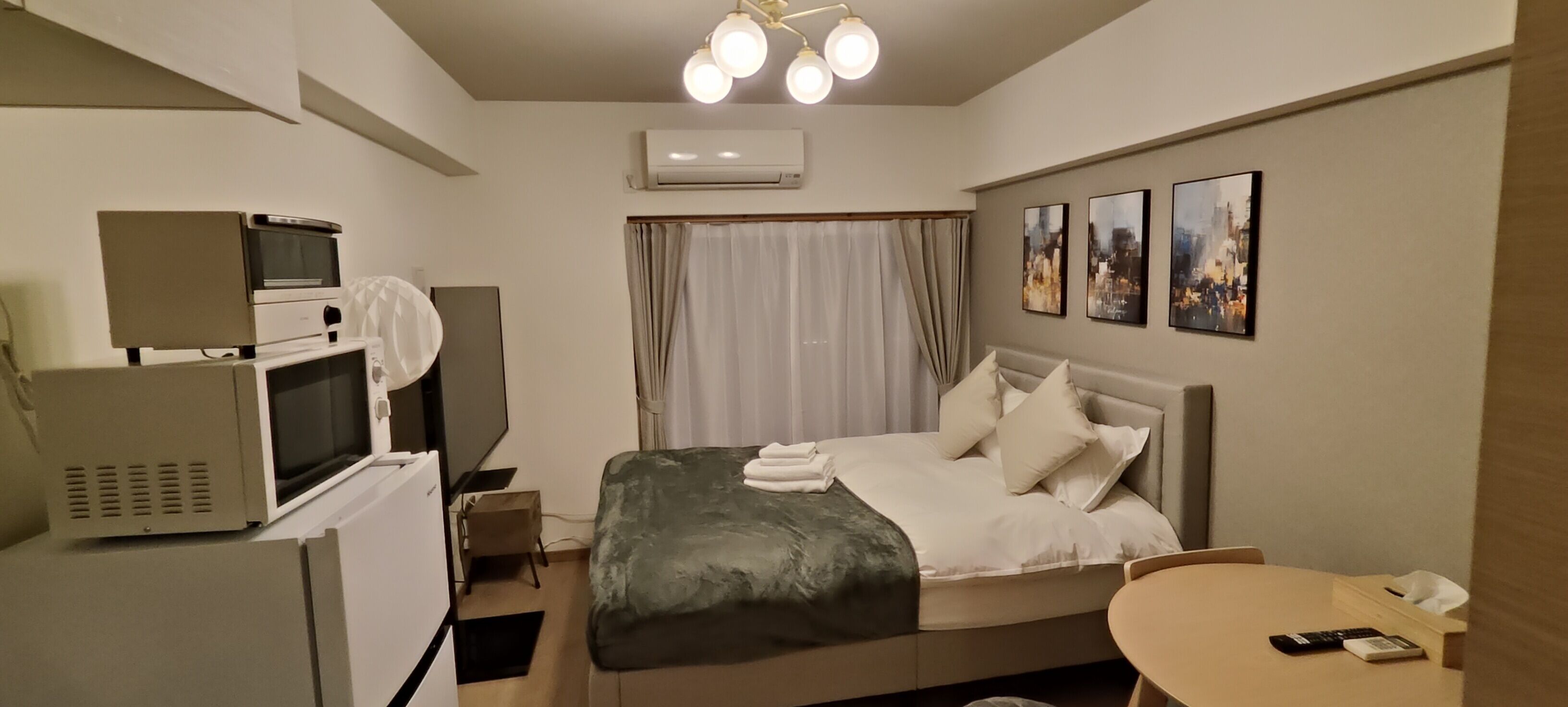 A hotel room with a bed, a desk, a microwave, an air conditioner, and a ceiling light fixture.