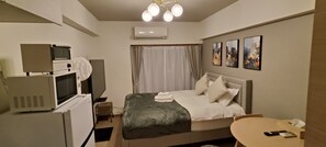 A hotel room with a bed, a desk, a microwave, an air conditioner, and a ceiling light fixture.