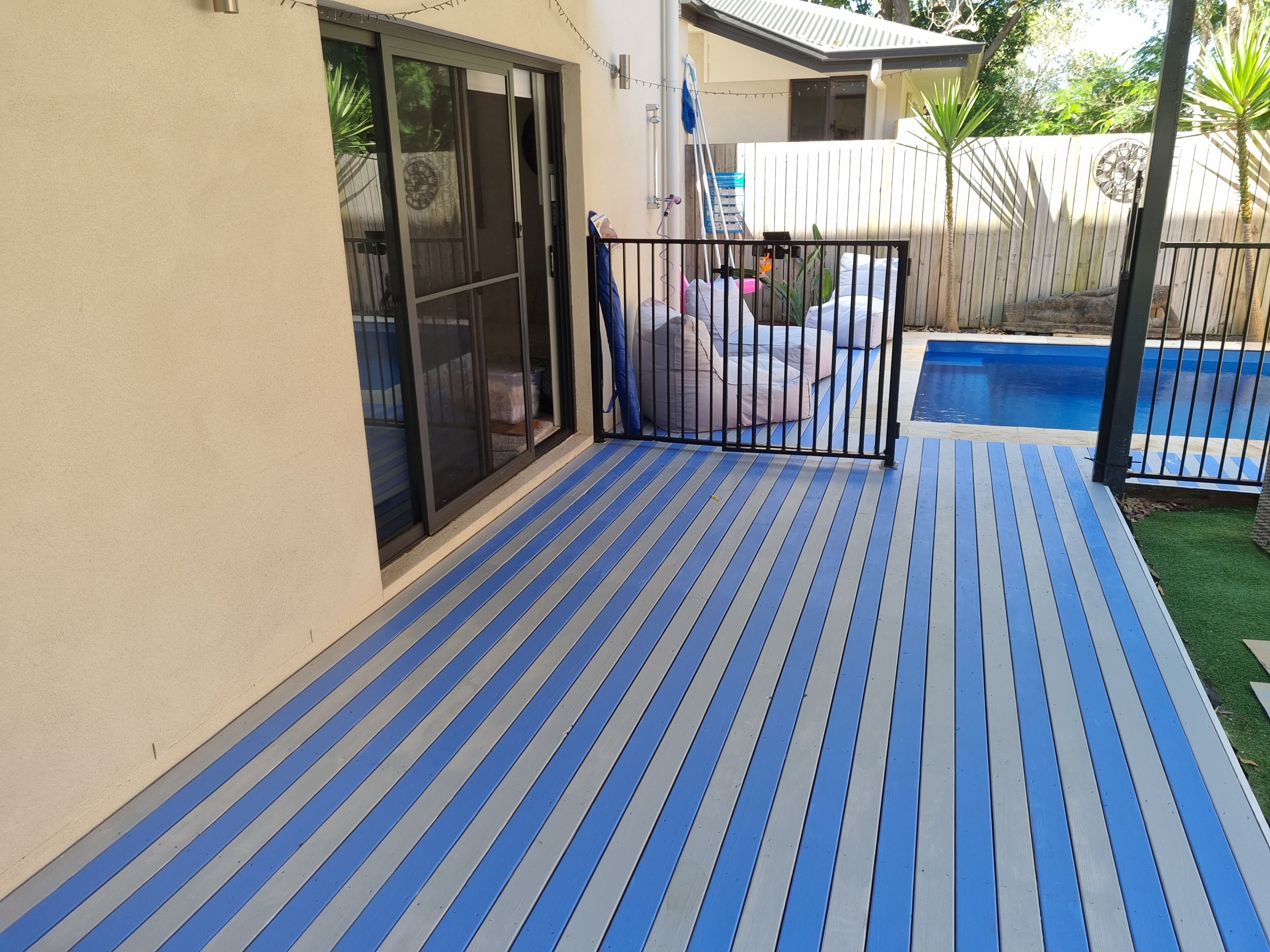 A covered patio with a blue and gray striped floor, a pool, and a wooden fence.