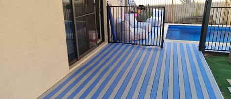 A covered patio with a blue and gray striped floor, a pool, and a wooden fence.