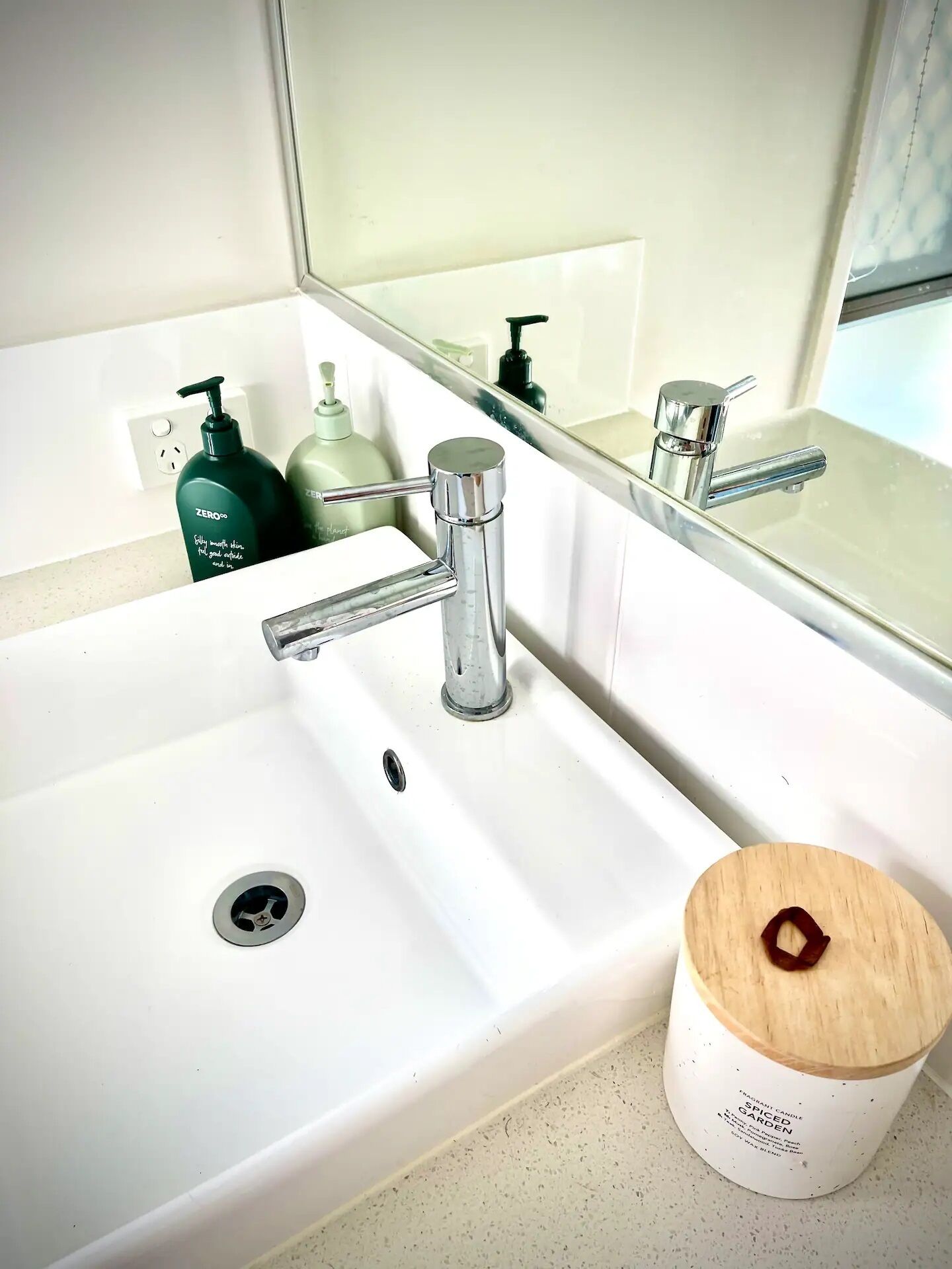 A bathroom sink with a chrome faucet, a mirror above it, and a candle on the countertop.
