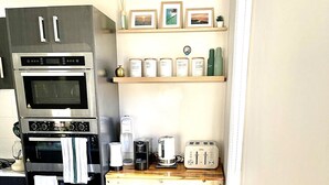 Una cocina compacta con horno integrado, cafetera, tostadora y un estante pequeño con fotografías enmarcadas.