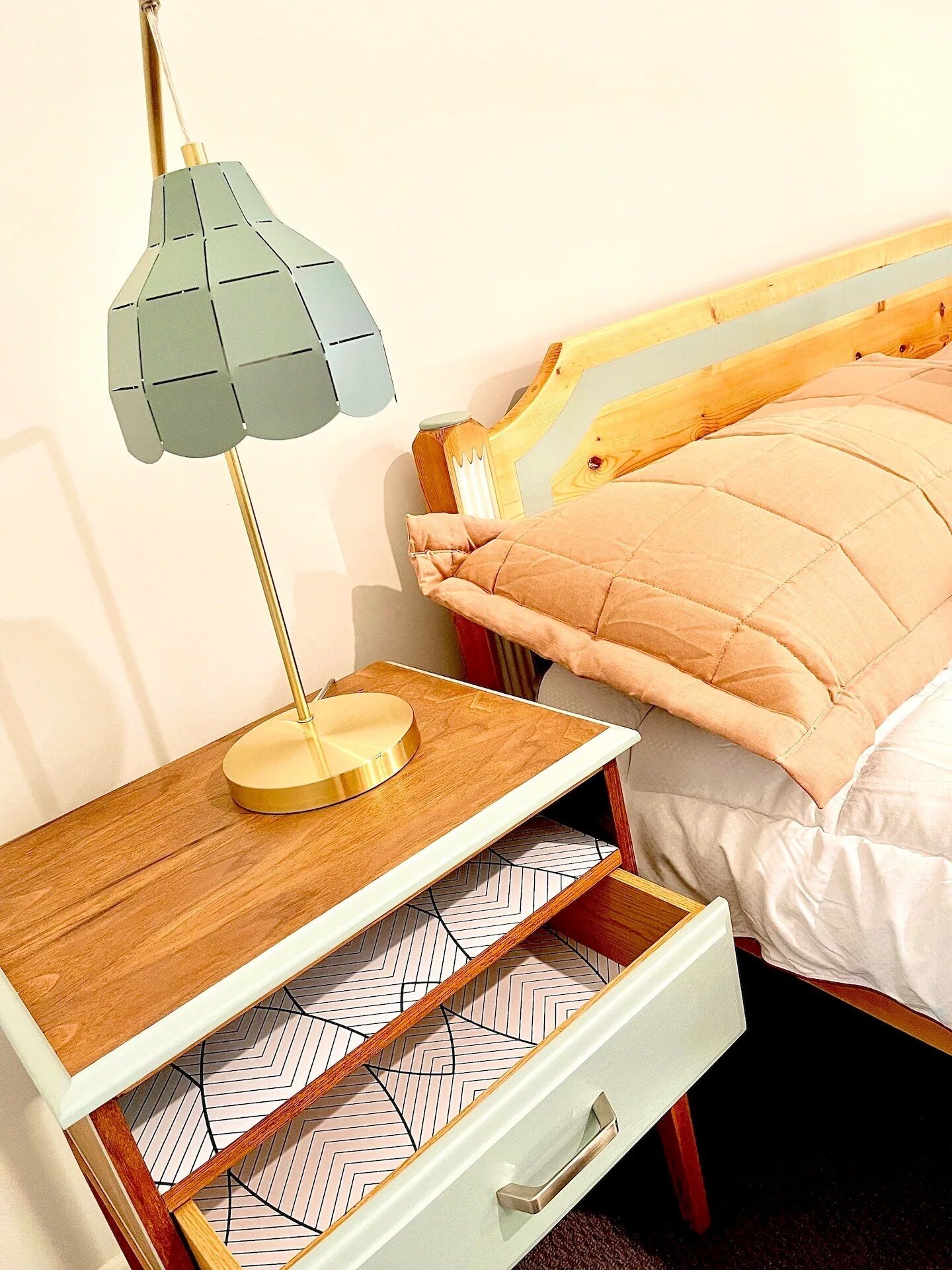 Una cama con cabecera de madera, una mesita de noche con lámpara y una cómoda con detalles de azulejos decorativos.