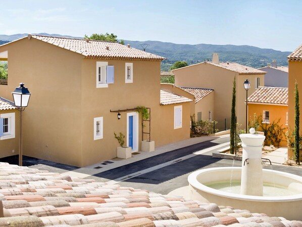 A residential street with houses, a fountain, and a mountainous backdrop.