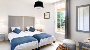 Ein Hotelzimmer mit zwei Betten, einem Schreibtisch, einem Stuhl, einer Hängeleuchte, einem mit Vorhängen versehenen Fenster und einem gerahmten Bild an der Wand.