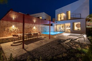 A modern house with a swimming pool, outdoor seating, and a stone wall. - Nisi Living Concep - Karpathos Villa (Ialysos)