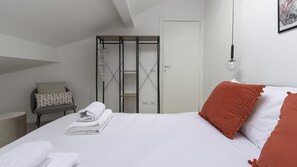 A neatly made bed with white and orange pillows, a folded towel, and a small table with a chair. - Italianway Easy - Settala 51 (Milan)