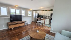 A modern living room with a flat-screen TV, wooden entertainment unit, and a round coffee table. - Light and breezy Kailua apartment (Kailua)