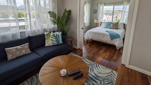 A room with a blue sofa, a round wooden coffee table, and a bed with a white and blue bedspread. - Light and breezy Kailua apartment (Kailua)