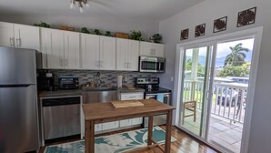 A modern kitchen with white cabinets, stainless steel appliances, and a wooden table. - Light and breezy Kailua apartment (Kailua)