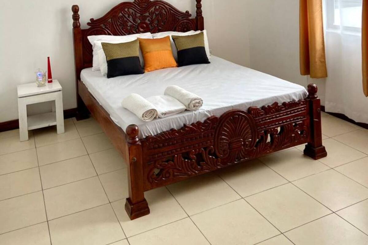 A neatly made bed with a wooden headboard, a small bedside table with a lamp, and a ceiling fan.