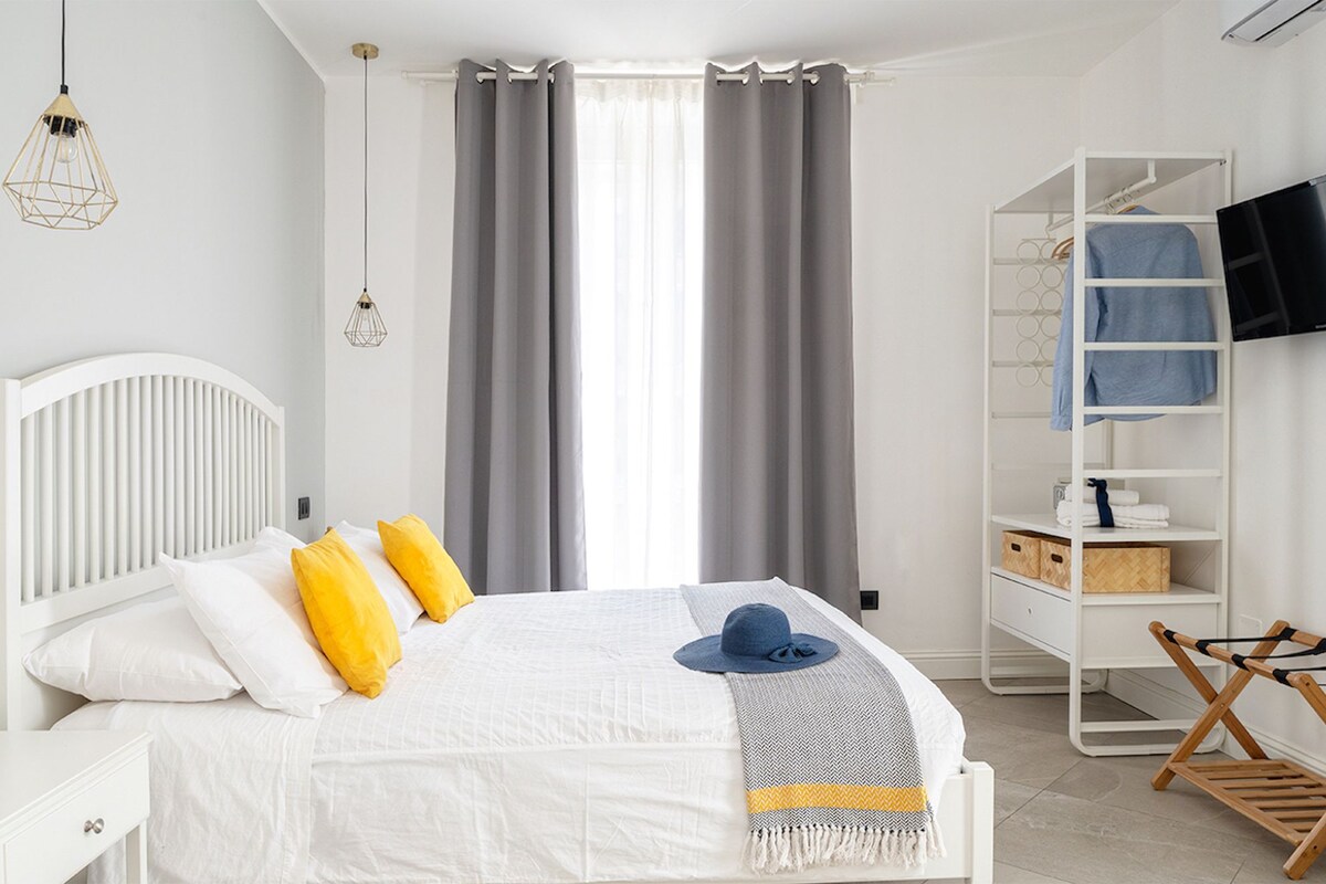 Un dormitorio moderno con una cama blanca, cortinas grises, un televisor montado en la pared y un tendedero de madera.