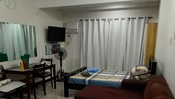 A living room with a sofa, a TV, a dining table, and a bed.