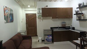 A compact kitchen with a refrigerator, sink, and cabinets. There's a brown sofa and a small table.