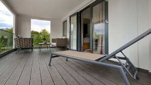 En balkon med liggestol, to polstrede stole og et lille bord.