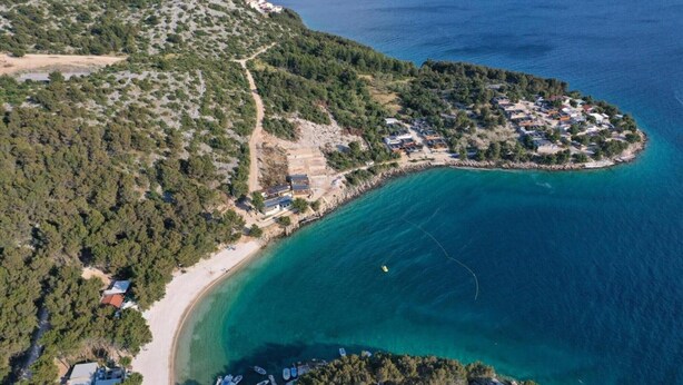 Oversigtsbillede af et kystområde med en strand, et lille bebyggelse med huse og både fortøjet nær kysten.