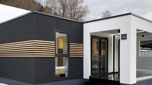 En moderne bygning med mørk facade, tydelig indgang og et vindue med vandrette trælister.