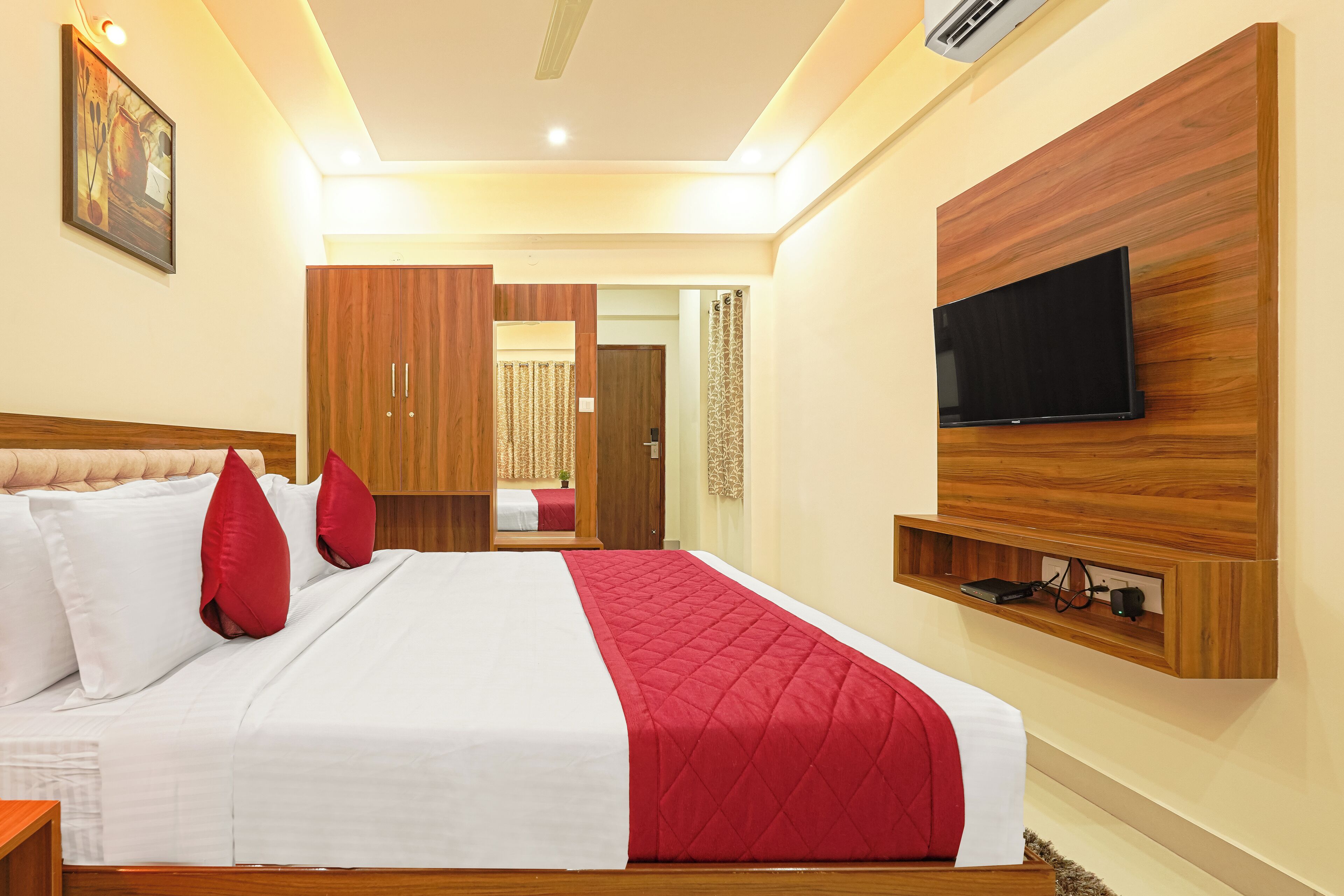 A hotel room with a large bed, a TV mounted on the wall, and a wooden wardrobe.