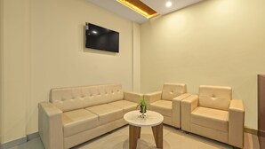 Una sala de estar moderna con un sofá color beige, dos sillones, una mesa de centro redonda y un televisor de pantalla plana montado en la pared.