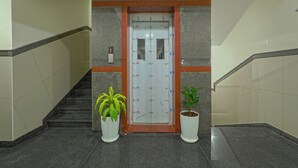 Un interior moderno con una escalera, una puerta con panel de vidrio y dos plantas en macetas.