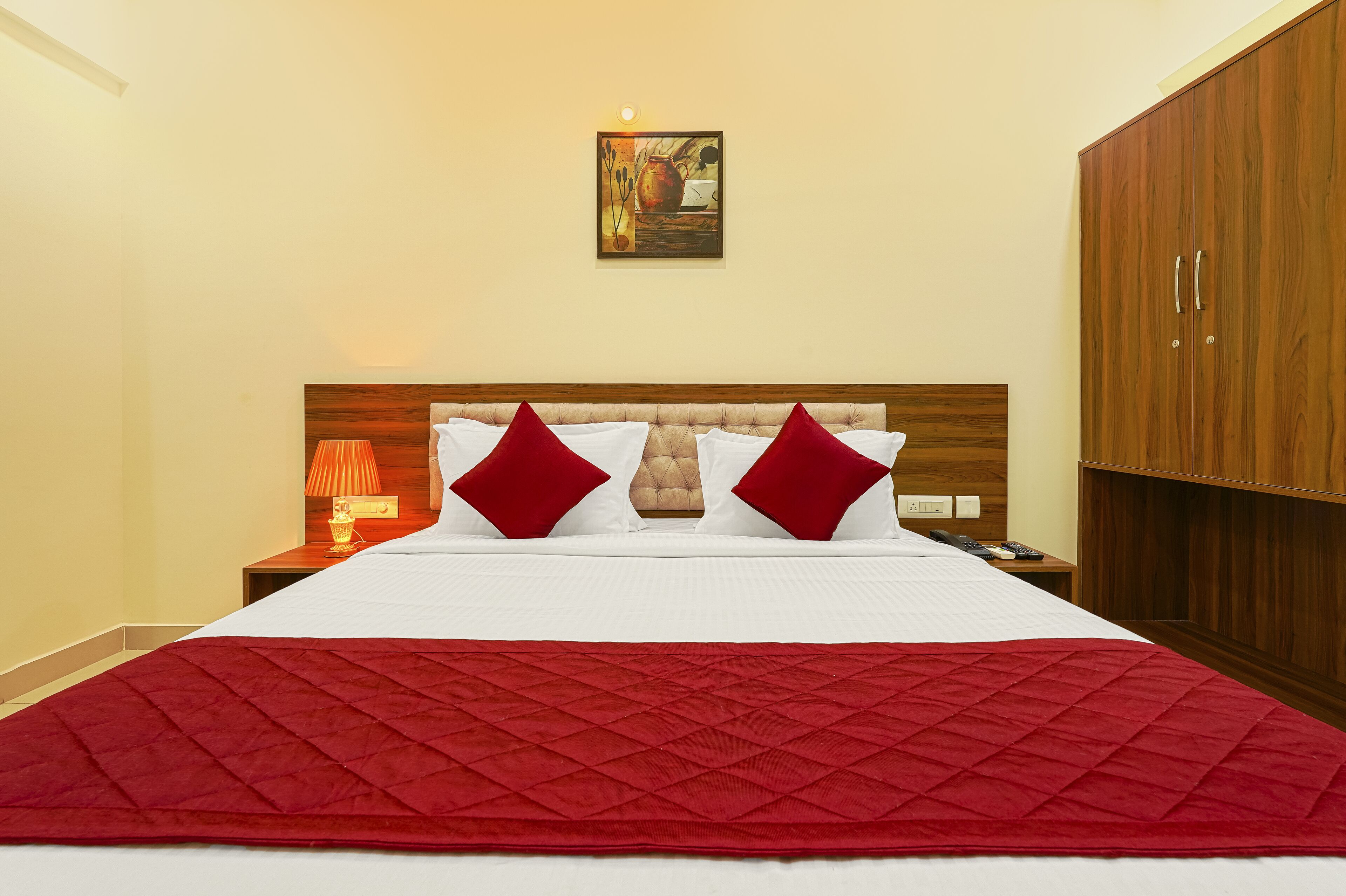 A neatly made bed with a red quilt, two red pillows, and a wooden headboard.