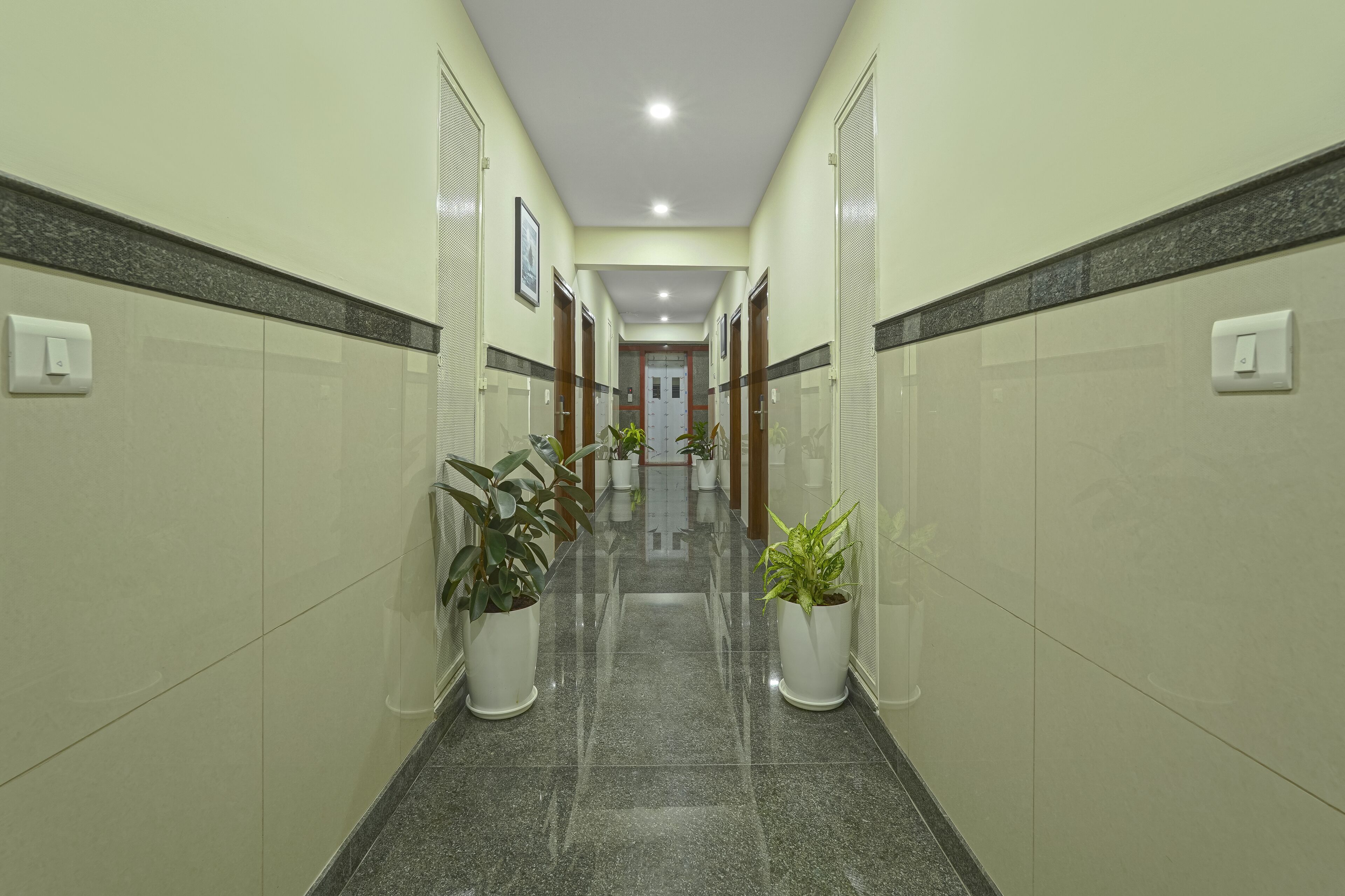 Um corredor com chão ladrilhado, plantas em vasos e portas de ambos os lados.