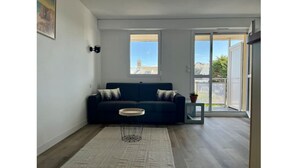 Un salon moderne avec un canapé bleu foncé, une petite table ronde et une grande fenêtre offrant une vue sur le paysage urbain.