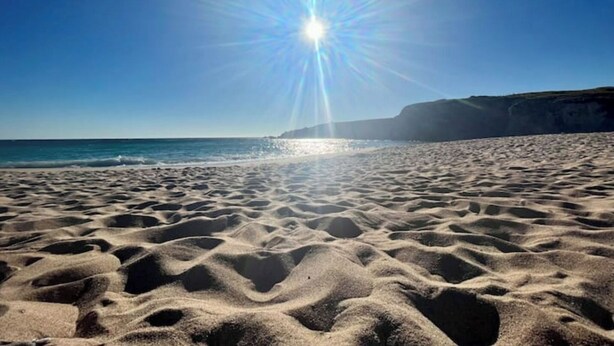 Une plage avec un ciel dégagé et la lumière du soleil qui se reflète sur le sable.