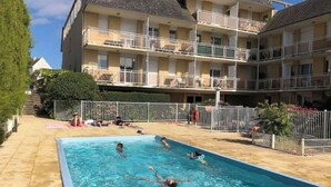 Une piscine entourée d’une zone délimitée par une clôture, avec un immeuble à plusieurs étages en arrière-plan.