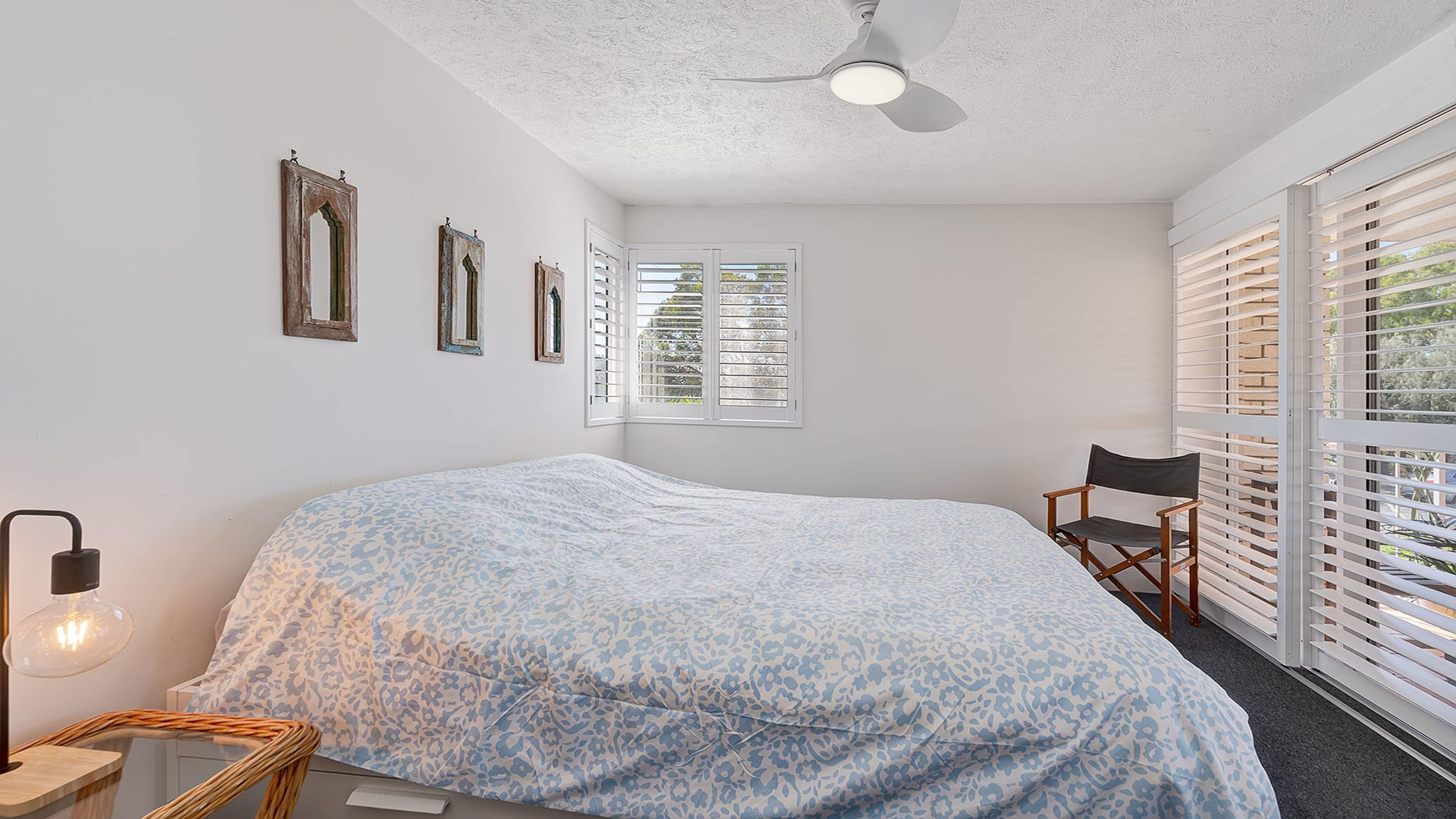 A bedroom with a bed, a chair, a ceiling fan, and a window with blinds.