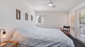 A bedroom with a bed, a chair, a ceiling fan, and a window with blinds. - Unit 1 Seascapes Golden Beach Waterfront Balcony (Golden Beach)
