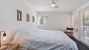 A bedroom with a bed, a chair, a ceiling fan, and a window with blinds.