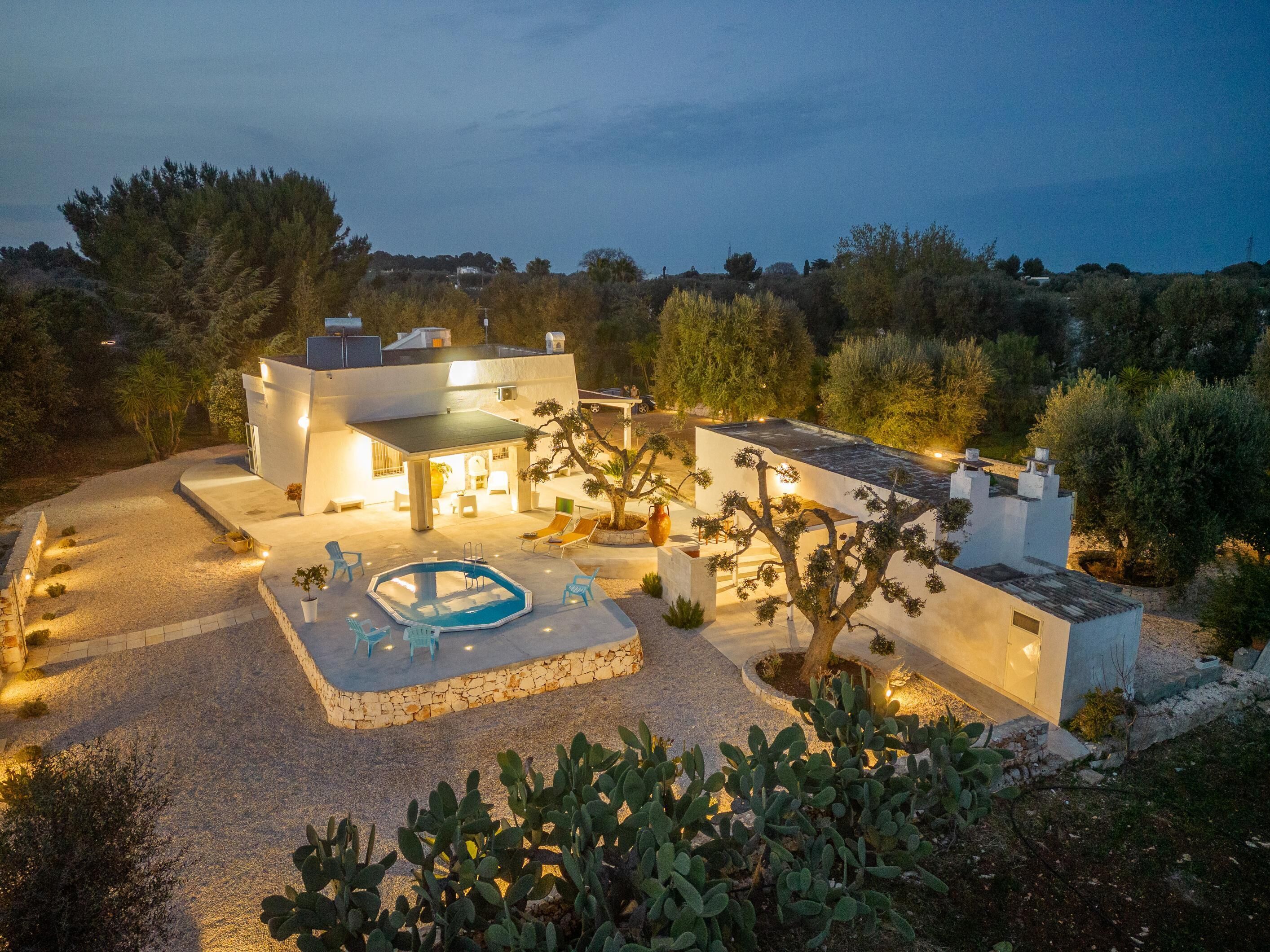 Une villa moderne dotée d’une piscine, d’un espace extérieur aménagé et d’un patio bien éclairé, le tout entouré de cactus et d’arbres.