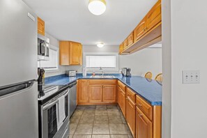 A compact kitchen with wooden cabinets, a built-in oven, a microwave, and a dishwasher. - Colchester Lake Getaway! (Colchester)