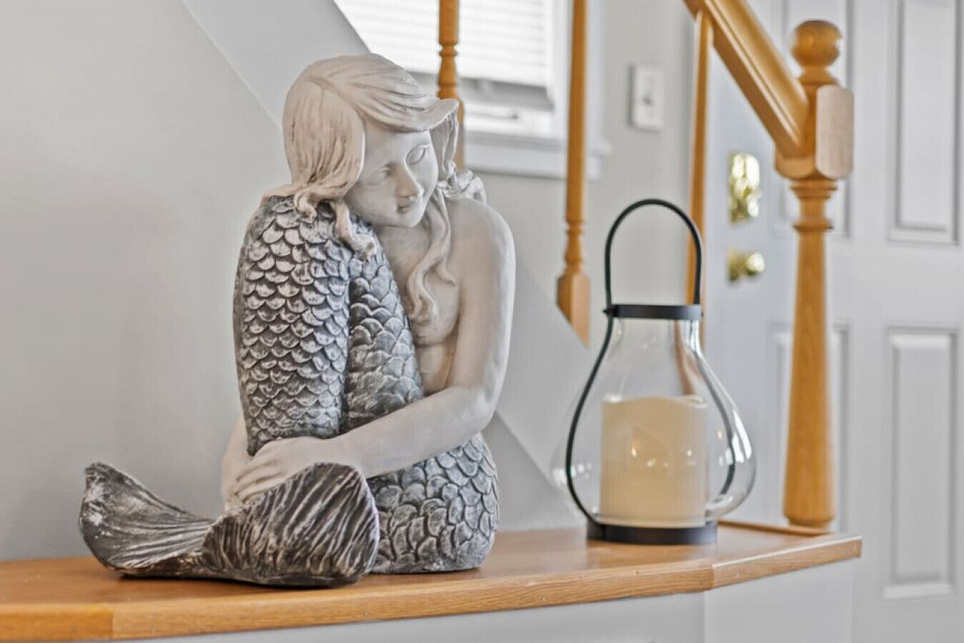 A statue of a mermaid sitting on a wooden ledge, next to a glass bottle with a candle.
