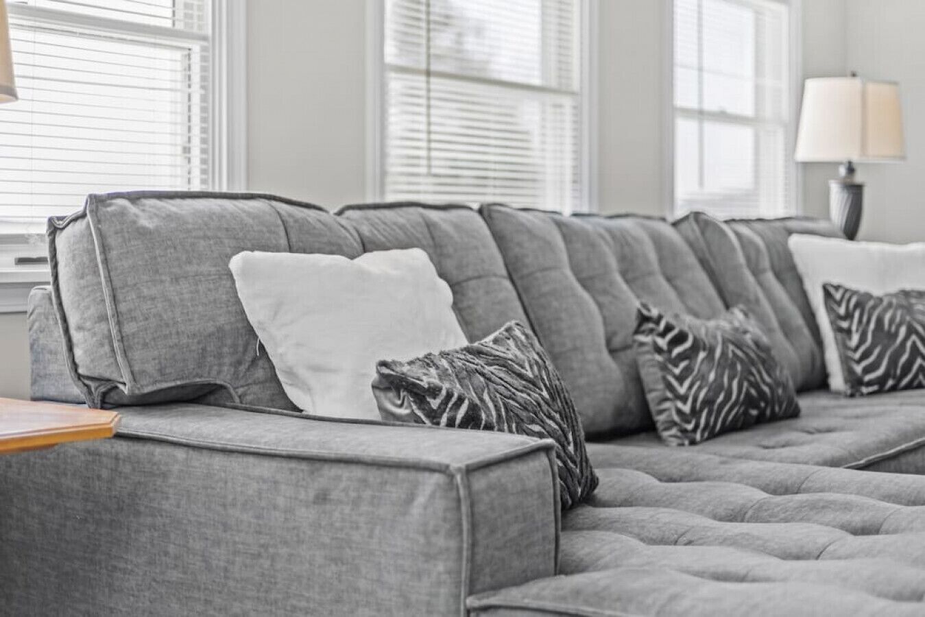 Ein graues Sofa mit gemusterten Kissen in einem Zimmer mit großen Fenstern und einer Lampe.